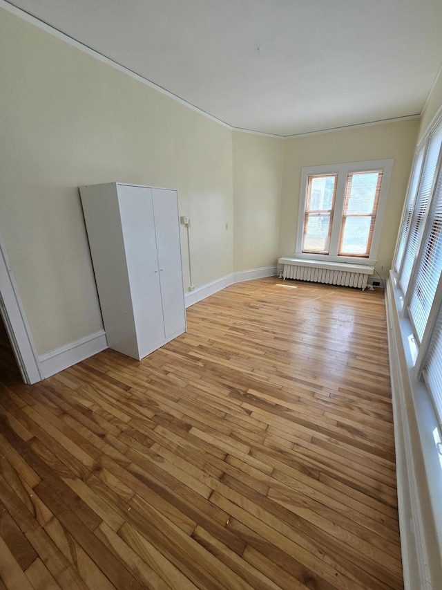 spare room featuring crown molding, radiator, light wood finished floors, and baseboards