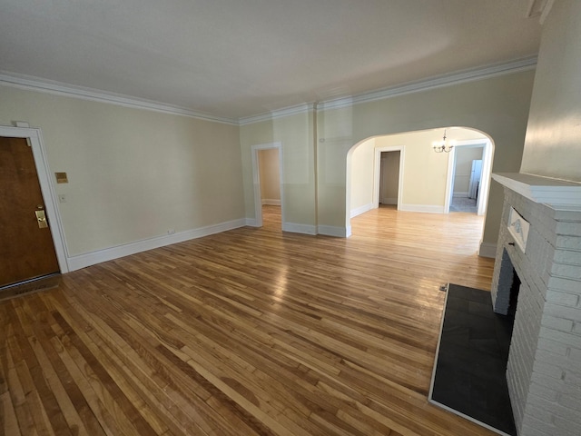 unfurnished living room featuring arched walkways, ornamental molding, and wood finished floors