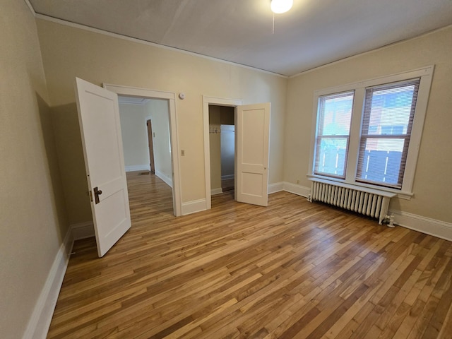 unfurnished bedroom featuring crown molding, light wood-type flooring, a closet, radiator heating unit, and baseboards