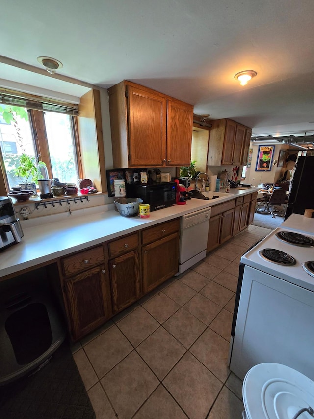 kitchen with light tile patterned floors, a sink, light countertops, white appliances, and brown cabinets
