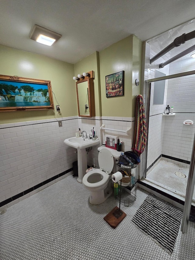 bathroom with a shower stall, toilet, a wainscoted wall, and tile walls