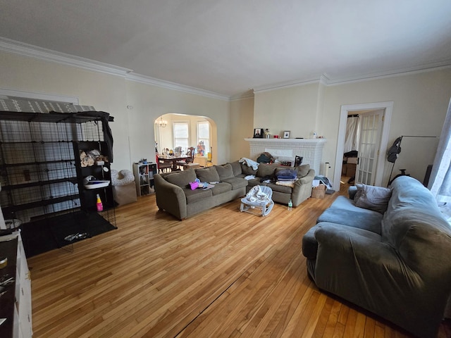 living area featuring light wood-style flooring, arched walkways, ornamental molding, and a brick fireplace
