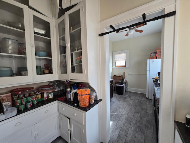 kitchen with freestanding refrigerator, dark countertops, a ceiling fan, dark wood finished floors, and white cabinetry