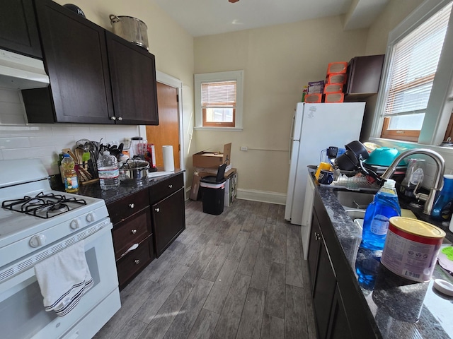 kitchen with dark stone counters, white appliances, under cabinet range hood, wood finished floors, and decorative backsplash