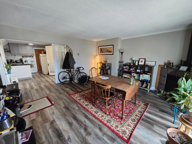 dining area with dark wood-type flooring, a textured ceiling, a baseboard radiator, and arched walkways
