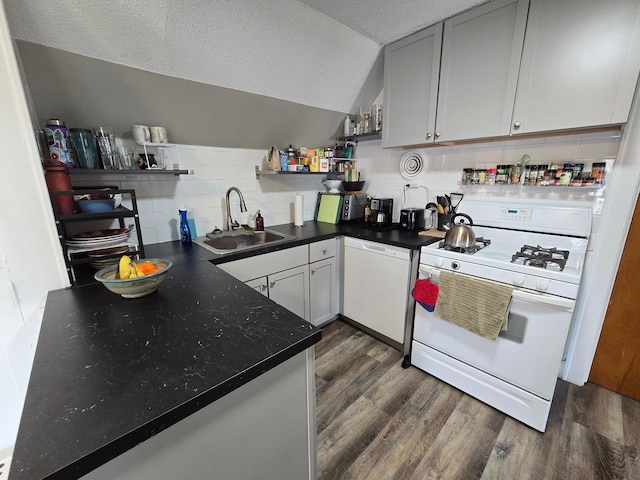 kitchen featuring white appliances, open shelves, dark countertops, dark wood finished floors, and a sink