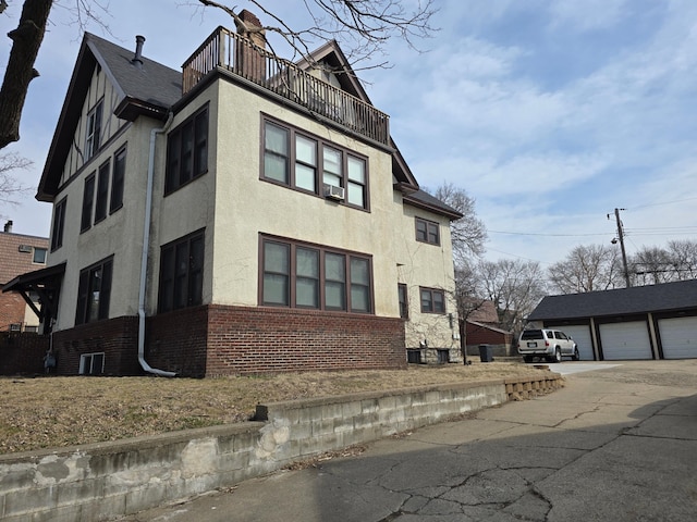 view of front of property featuring an outbuilding, stucco siding, brick siding, a chimney, and a balcony