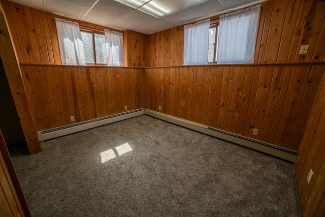 carpeted empty room featuring a wealth of natural light, wood walls, a paneled ceiling, and a baseboard heating unit