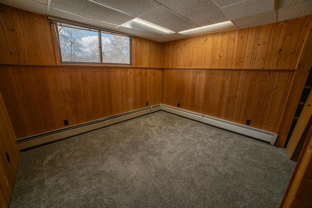 carpeted spare room featuring wooden walls, a paneled ceiling, and baseboard heating