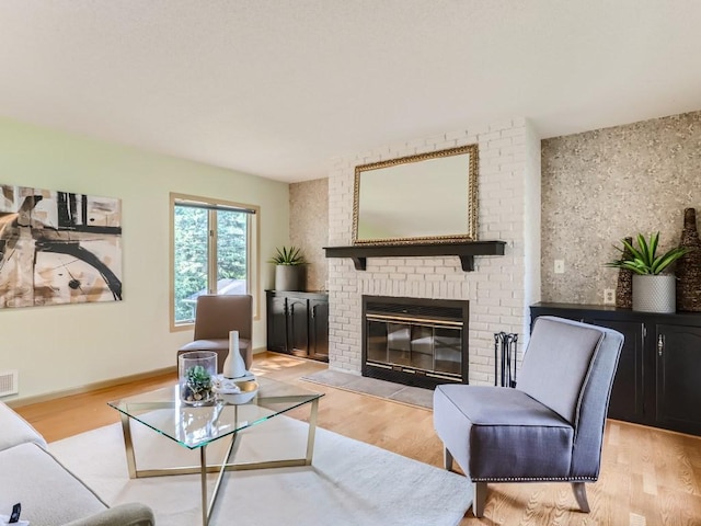 living room with a brick fireplace, visible vents, and light wood-style floors
