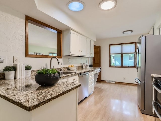 kitchen with light stone countertops, white cabinetry, a sink, light wood-style flooring, and stainless steel appliances