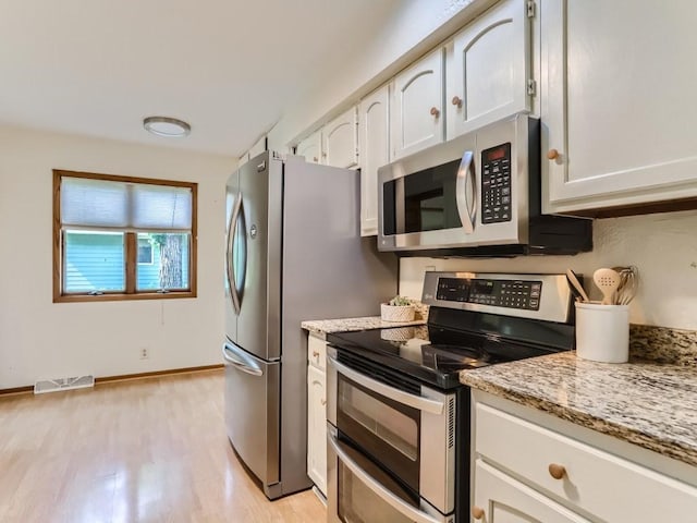 kitchen featuring white cabinets, light stone countertops, appliances with stainless steel finishes, light wood-type flooring, and visible vents