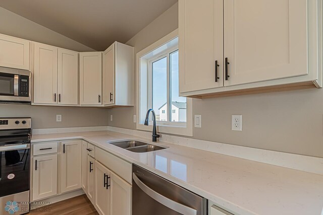 kitchen featuring vaulted ceiling, white cabinets, wood finished floors, a sink, and stainless steel appliances