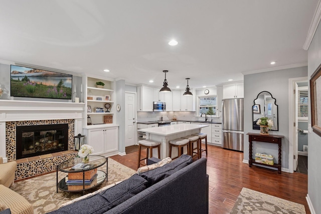 living area with crown molding, dark wood finished floors, a tile fireplace, baseboards, and recessed lighting