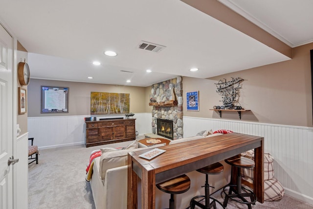 living room featuring wainscoting, carpet floors, a stone fireplace, visible vents, and ornamental molding