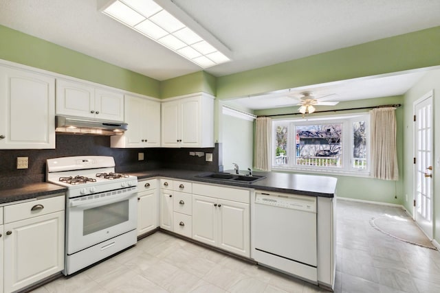 kitchen with dark countertops, a sink, white cabinets, under cabinet range hood, and white appliances