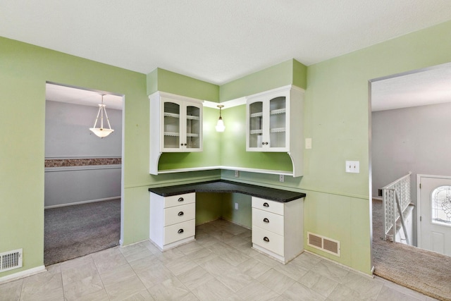 interior space with white cabinets, visible vents, glass insert cabinets, and built in study area