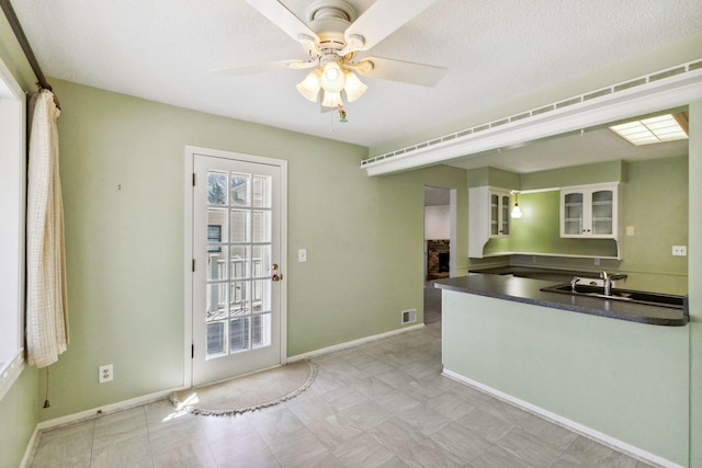 kitchen featuring a ceiling fan, dark countertops, a sink, baseboards, and glass insert cabinets
