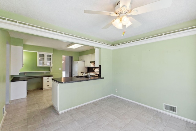 kitchen featuring visible vents, freestanding refrigerator, dark countertops, white cabinets, and a sink