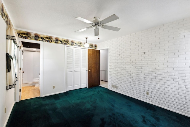 unfurnished bedroom with carpet floors, a closet, brick wall, connected bathroom, and a ceiling fan