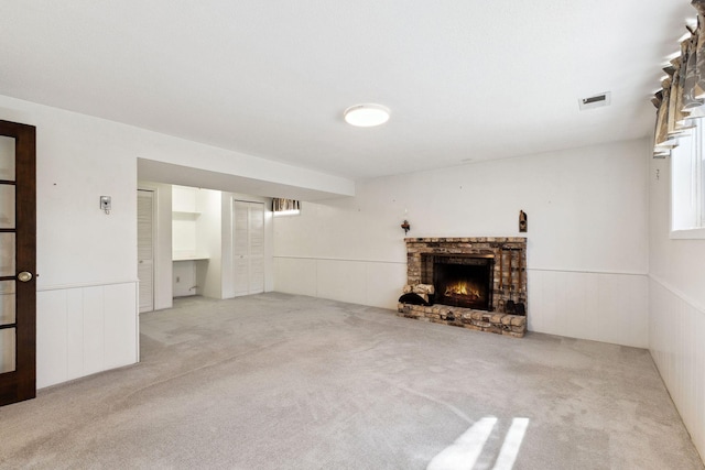 unfurnished living room with carpet floors, visible vents, a wainscoted wall, and a fireplace