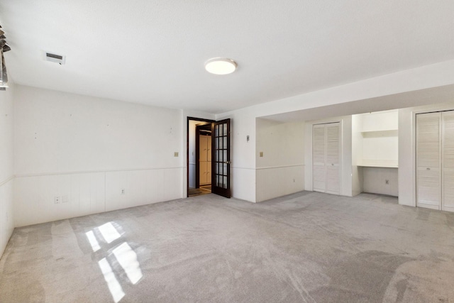 unfurnished bedroom featuring visible vents, carpet, and two closets