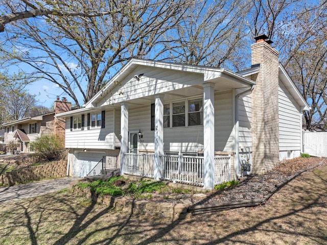 raised ranch with covered porch, a chimney, an attached garage, and driveway