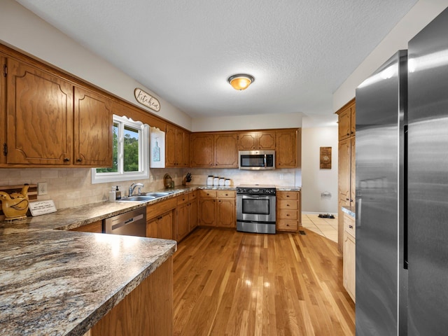 26635 Variolite St NW, Stanford Twp, MN 55070 - kitchen with appliances with stainless steel finishes, brown cabinets, decorative backsplash, light wood finished floors, and a textured ceiling