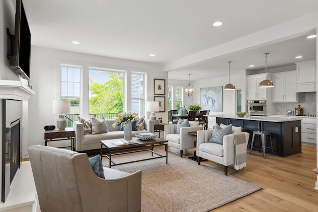 living area with a glass covered fireplace, recessed lighting, and light wood finished floors