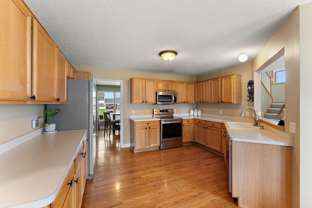 kitchen with light countertops, a sink, light wood finished floors, and stainless steel appliances