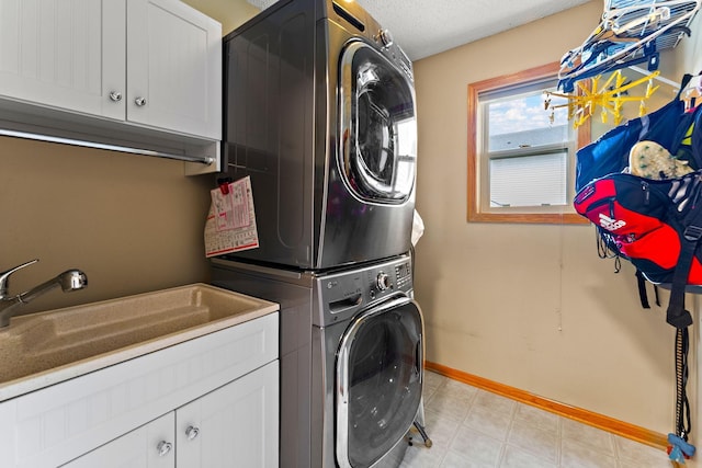 clothes washing area with baseboards, a sink, cabinet space, and stacked washer / drying machine