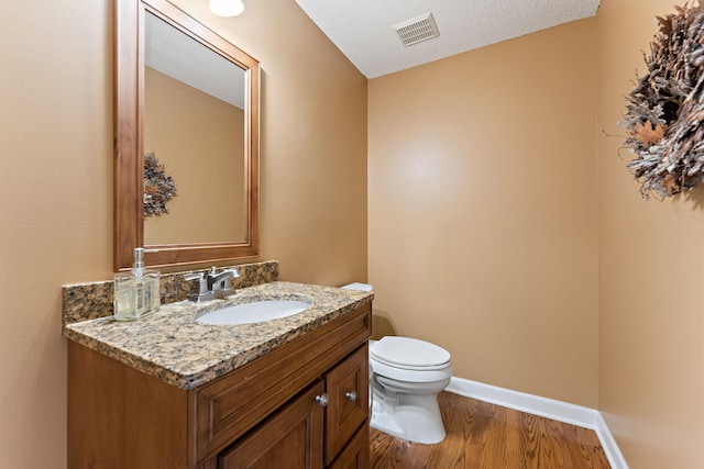 half bath featuring visible vents, wood finished floors, vanity, baseboards, and toilet