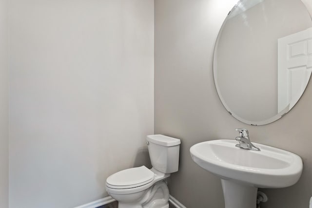 half bathroom with baseboards, toilet, and a sink