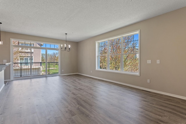 unfurnished dining area with a chandelier, dark wood-type flooring, baseboards, and a textured ceiling