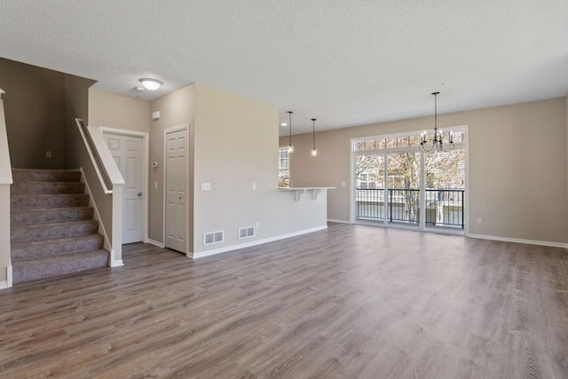 unfurnished living room with a chandelier, wood finished floors, baseboards, a textured ceiling, and stairway