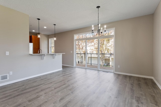 unfurnished living room featuring baseboards, wood finished floors, a chandelier, recessed lighting, and a textured ceiling