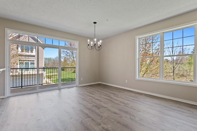 unfurnished room with a chandelier, baseboards, wood finished floors, and a textured ceiling