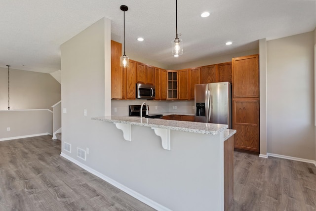 kitchen featuring appliances with stainless steel finishes, a peninsula, light wood finished floors, a kitchen breakfast bar, and light stone counters