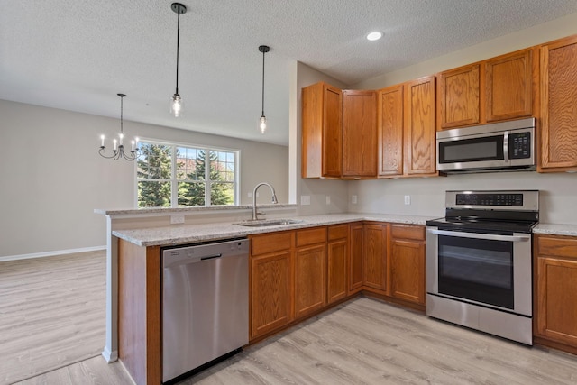 kitchen featuring appliances with stainless steel finishes, a sink, a textured ceiling, light wood finished floors, and brown cabinets