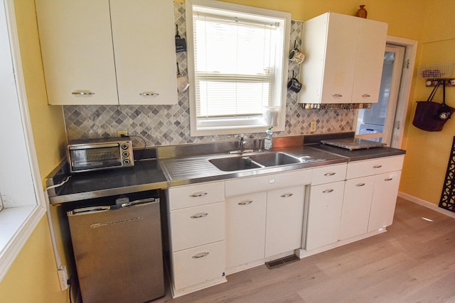 kitchen featuring white cabinets, dishwashing machine, a sink, and stainless steel countertops