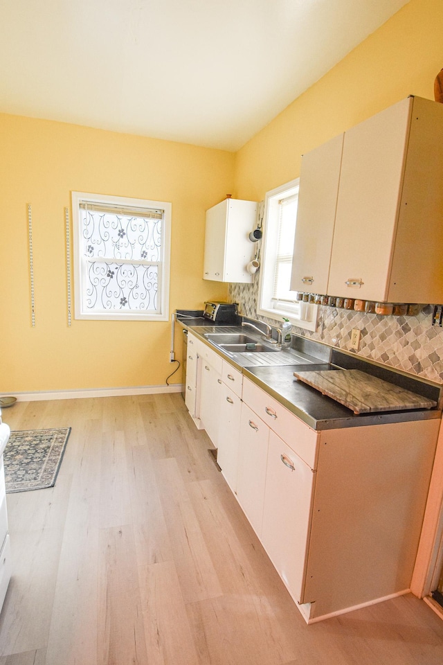 kitchen featuring range with electric stovetop, a sink, light wood finished floors, stainless steel counters, and decorative backsplash