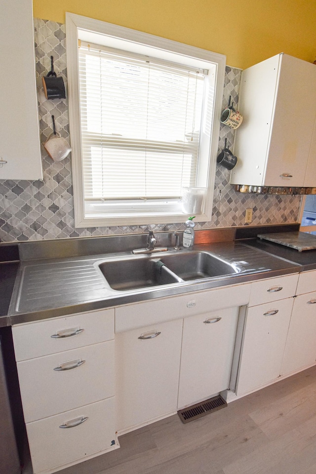 kitchen featuring a sink, stainless steel counters, tasteful backsplash, and white cabinets