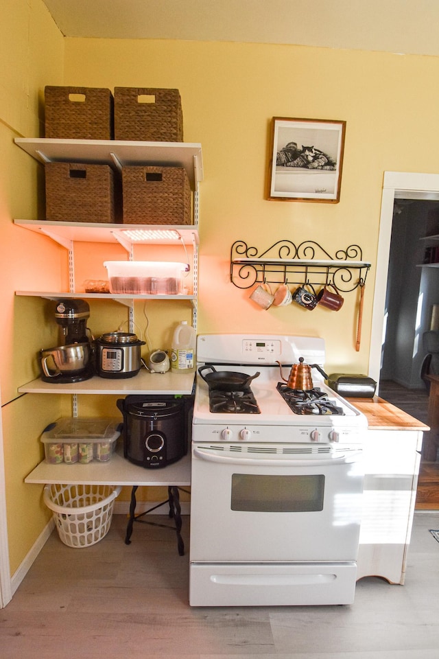 kitchen featuring baseboards, white range with gas cooktop, and wood finished floors