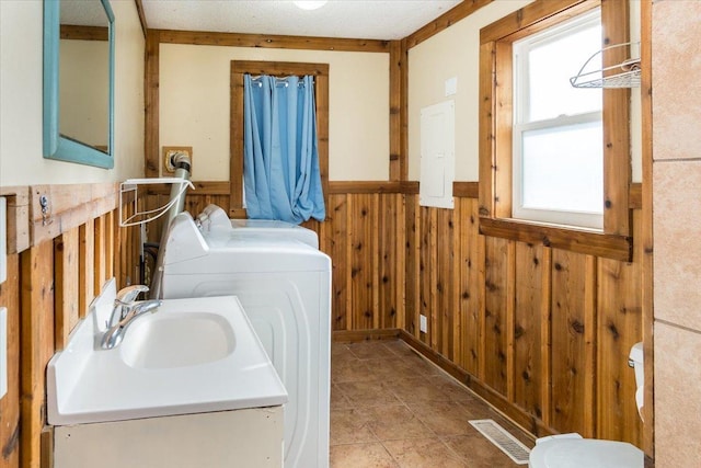bathroom featuring washing machine and dryer, toilet, a wainscoted wall, wood walls, and visible vents