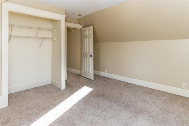 unfurnished bedroom featuring a closet, baseboards, lofted ceiling, and carpet floors