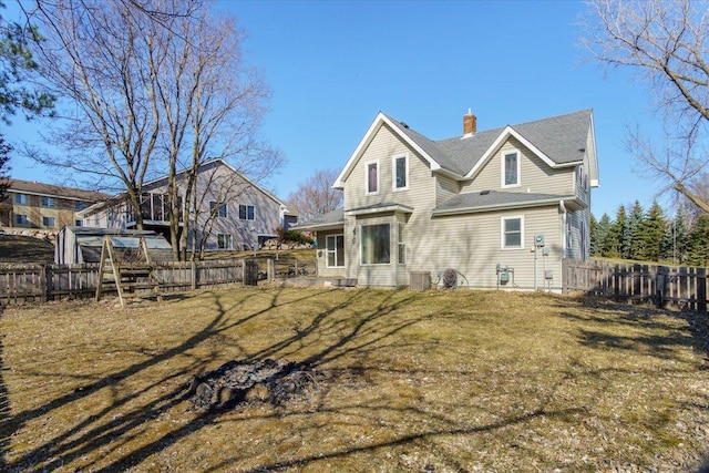 rear view of house featuring a yard, a fenced backyard, and a chimney
