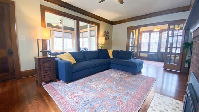 living area featuring baseboards, ornamental molding, a fireplace, wood finished floors, and a ceiling fan
