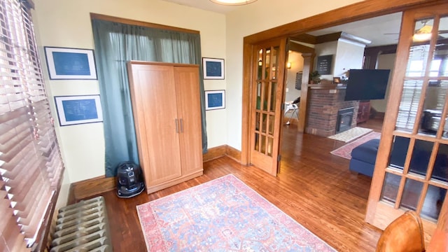 foyer entrance with wood finished floors, radiator heating unit, a fireplace, baseboards, and french doors
