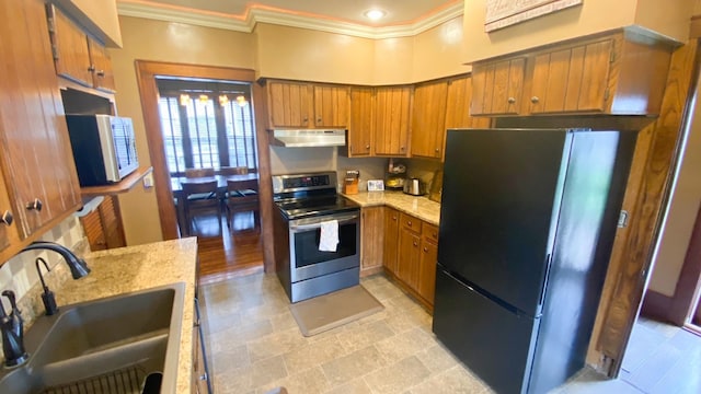 kitchen featuring under cabinet range hood, appliances with stainless steel finishes, brown cabinets, a sink, and crown molding