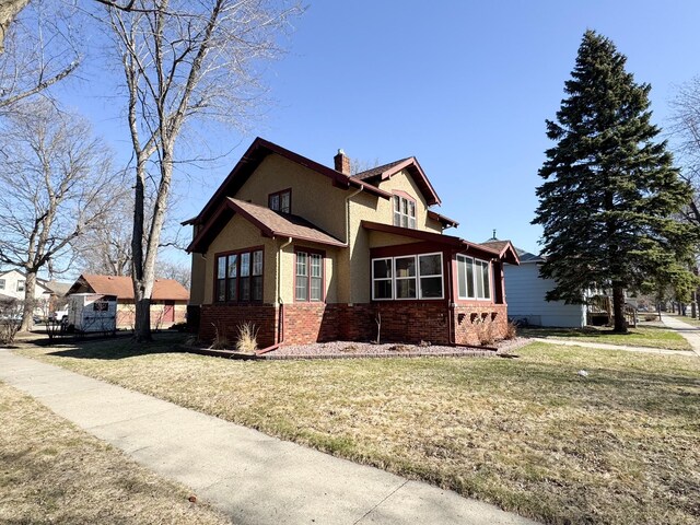 view of property exterior with a chimney, brick siding, stucco siding, and a yard